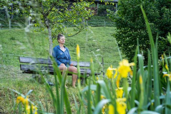 Auf dem Bild ist eine Frau zu sehen, die in der Natur sitzt und meditiert. 